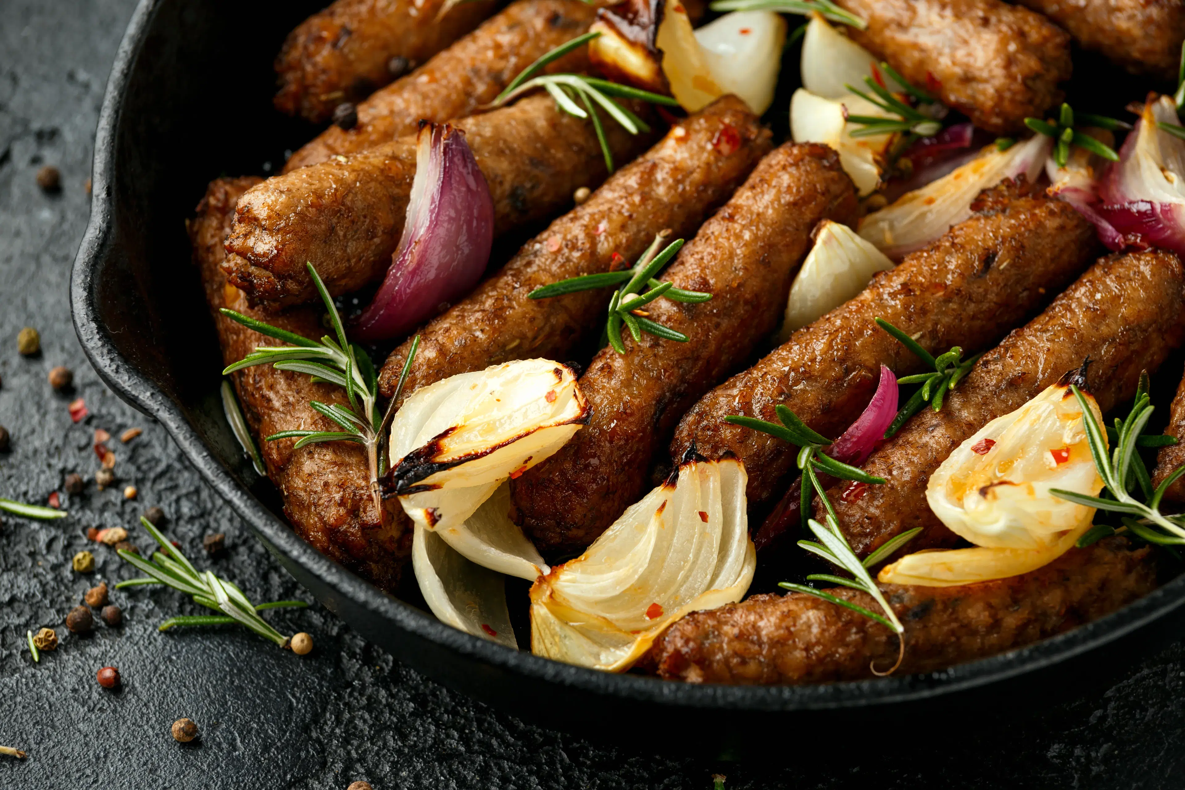 Sausages in a skillet with rosemary and onions